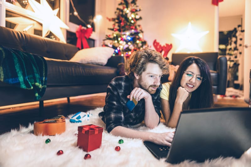 Couple laying on the floor looking at a laptop with Christmas decorations in the background